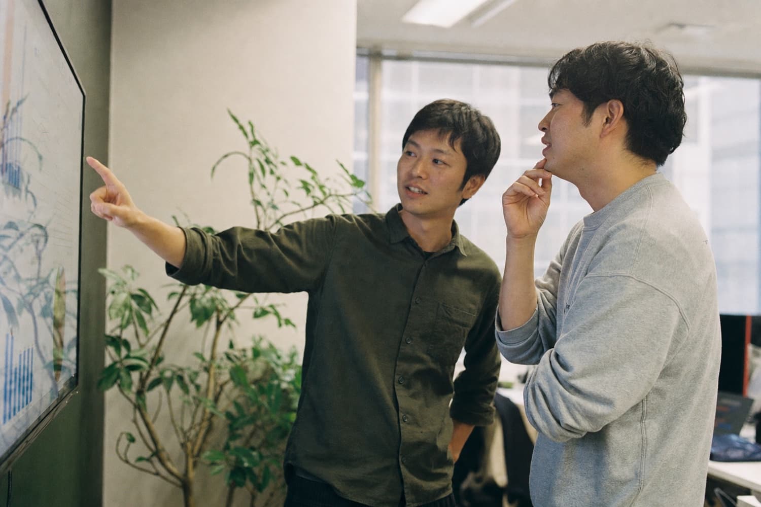 大きな画面のデータを指さして話し合うメンバー